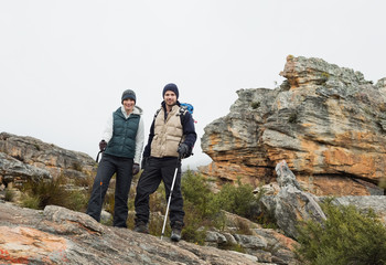 Couple standing on rocky landscape with trekking poles against c