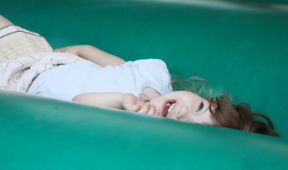 Little beautiful happy girl lies on green bouncy castle