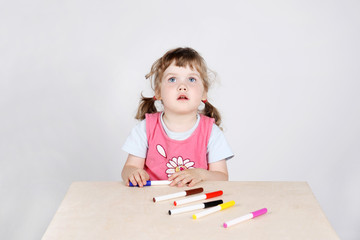 Little cute girl sits at table with felt-tip pens