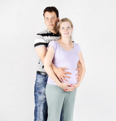 Fototapeta premium Handsome man hugs belly of pregnant woman on grey background.