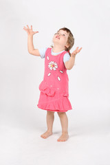 Little barefoot girl in pink with raised hands looks up on white