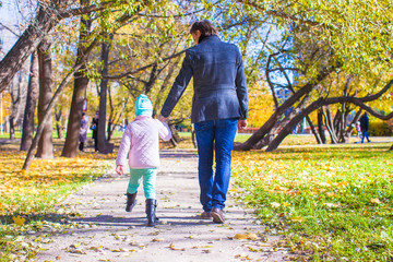 Fototapeta premium Rear view of young father and little girl walking in autumn park