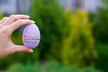 Bright purple Easter egg in hand on background of blue sky