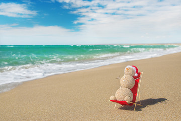 Sandy snowman in santa hat sunbathing in beach lounge. Holiday c