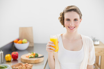 Obraz na płótnie Canvas Beautiful woman posing in her kitchen holding a glass of orange