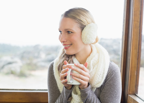 Smiling woman wearing earmuff with coffee cup against window