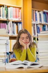 Tired beautiful student studying between piles of books with clo
