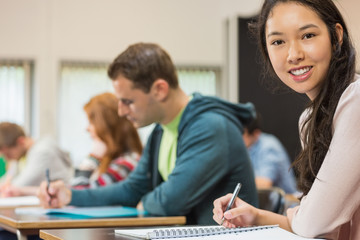 Female student with others writing notes in classroom