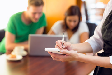 Mid section of a waitress writing order with students using lapt