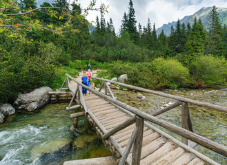 Fototapeta na wymiar Stream and family on wooden bridge (High Tatras, Slovakia) .