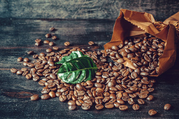Grains of roasted coffee with green leaves  on a wooden board