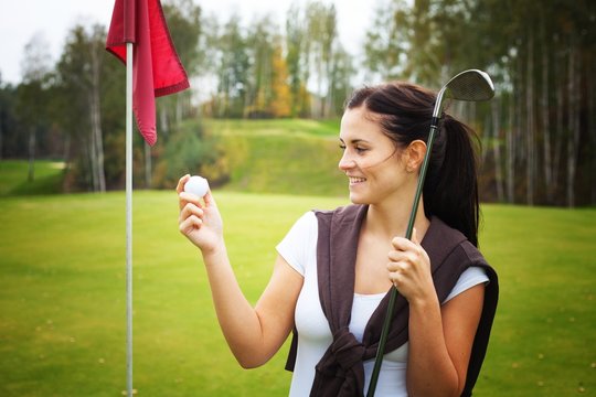 Young woman golf player looking at ball with club