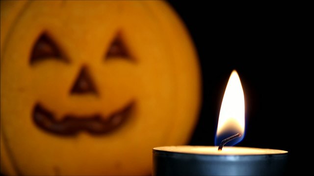 Candle burns in front of Halloween pumpkin