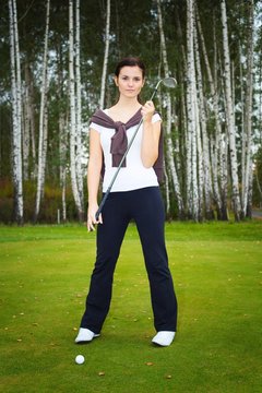 Woman golf player posing on green with club and ball