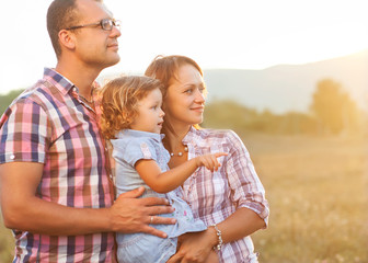 Fototapeta premium Happy mother, father and daughter in sunset