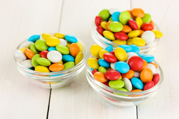 Colorful candies in glass bowls on white wooden background