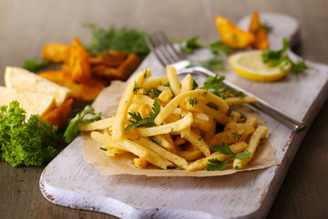 French fries on tracing paper on board on wooden table