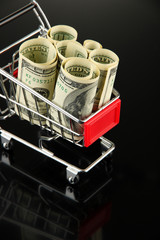 Shopping trolley with dollars, on dark background
