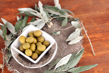 Olives in bowl with branch on sackcloth on wooden table