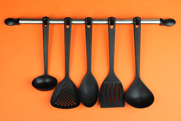Plastic kitchen utensils on silver hooks on orange background