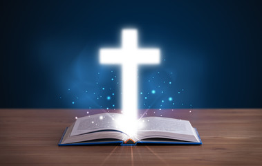 Open holy bible with glowing cross in the middle