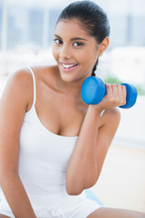 Cheerful toned brunette sitting on floor with dumbbells