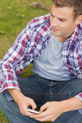 Obraz premium Handsome content student sitting on grass texting