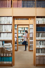 Full length of a female student reading a book in library