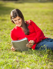 Woman Reading Book While Relaxing On Grass At Campus