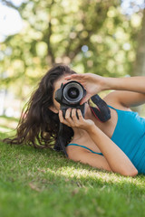 Young brunette woman lying on a lawn taking a picture