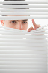 Serious male eyes spying through roller blind