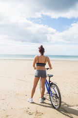Fototapeta na wymiar Slender woman standing with bike on the beach