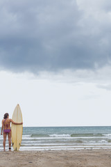 Calm woman in bikini with surfboard on beach