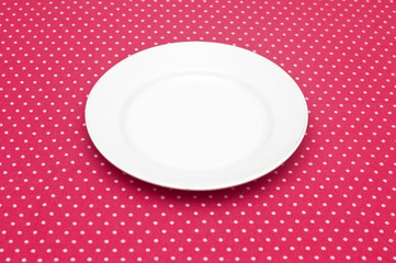 Empty white dinner plate on fun red polka dot tablecloth.