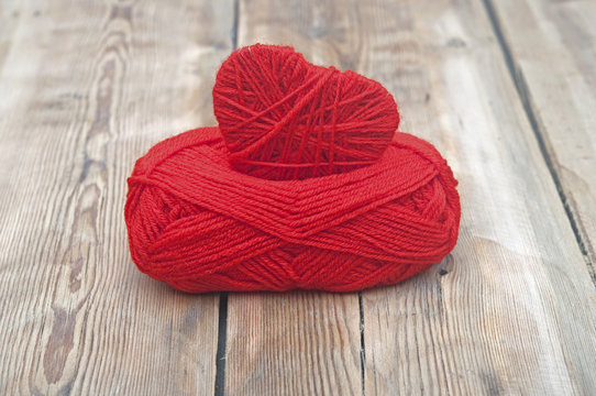 Knitted heart and red of yarn on wood background