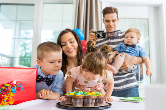 Family Watching Girl Blowing Out Candles On Birthday Cake