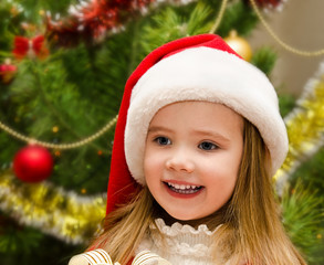 Cute little girl in santa hat near the christmas tree