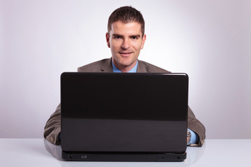 young business man smiles from behind laptop