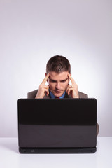 young business man looks at laptop with fingers at temples