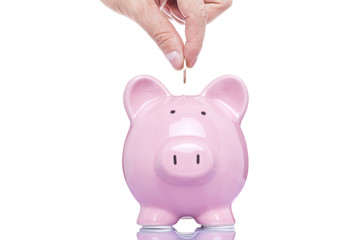 Hand inserting a coin into pink piggy bank, isolated on white ba