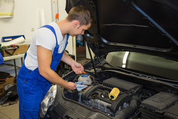 Mechanic in garage checking motor oil level at a car