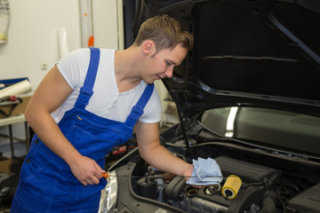 Fototapeta na wymiar Mechanic in garage checking motor oil level at a car