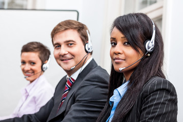 Callcenter Mitarbeiter mit Kopfhörern am Computer freundlich