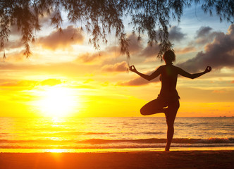 Fototapeta na wymiar Young woman practicing yoga on the beach. Silhouette at sunset.