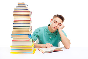 Young tired student sitting at the desk with high books stack