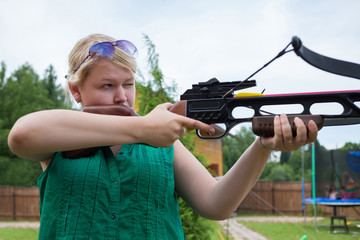 A girl with a crossbow in hands aiming at a target