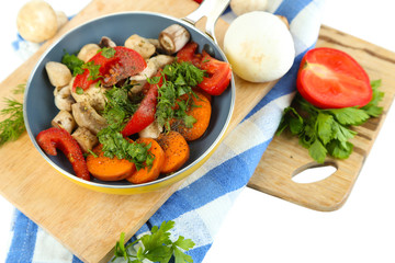 Sliced fresh vegetables in pan on wooden board isolated on
