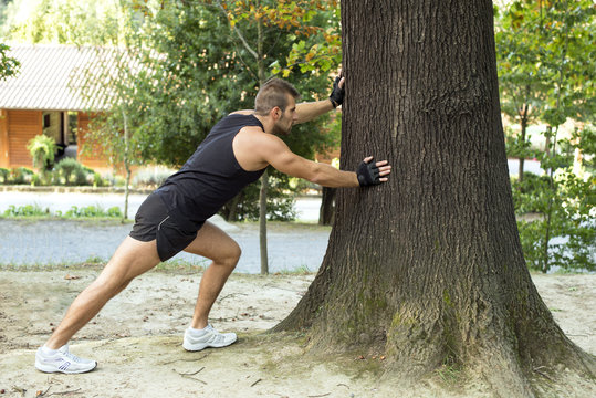 Sporty man doing stretching leaning the big trree.
