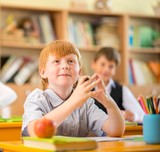 Little redhead schoolboy behind school desk