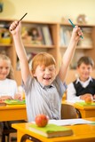 Little redhead schoolboy behind school desk during lesson